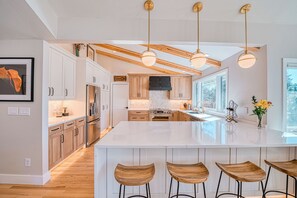 Una cocina moderna con armarios de madera, una isla grande con taburetes de bar, iluminación colgante y vistas al exterior.