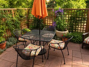 A patio with a metal table and chairs, surrounded by potted plants and a wooden fence.