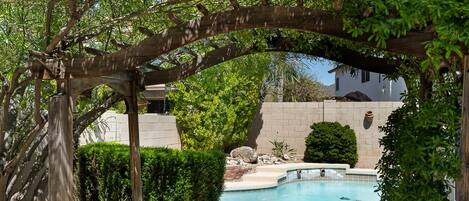 Un sendero de piedra que conduce a un área de piscina con una pérgola de madera.