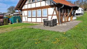 A traditional half-timbered house with a sloped roof, a patio with outdoor furniture, and a grassy yard. - HM - Holiday home 3 Deluxe Krombachtalsperre Westerwald (Driedorf)