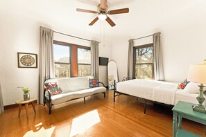 Una habitación con cama, sofá, ventilador de techo y ventana con cortinas.