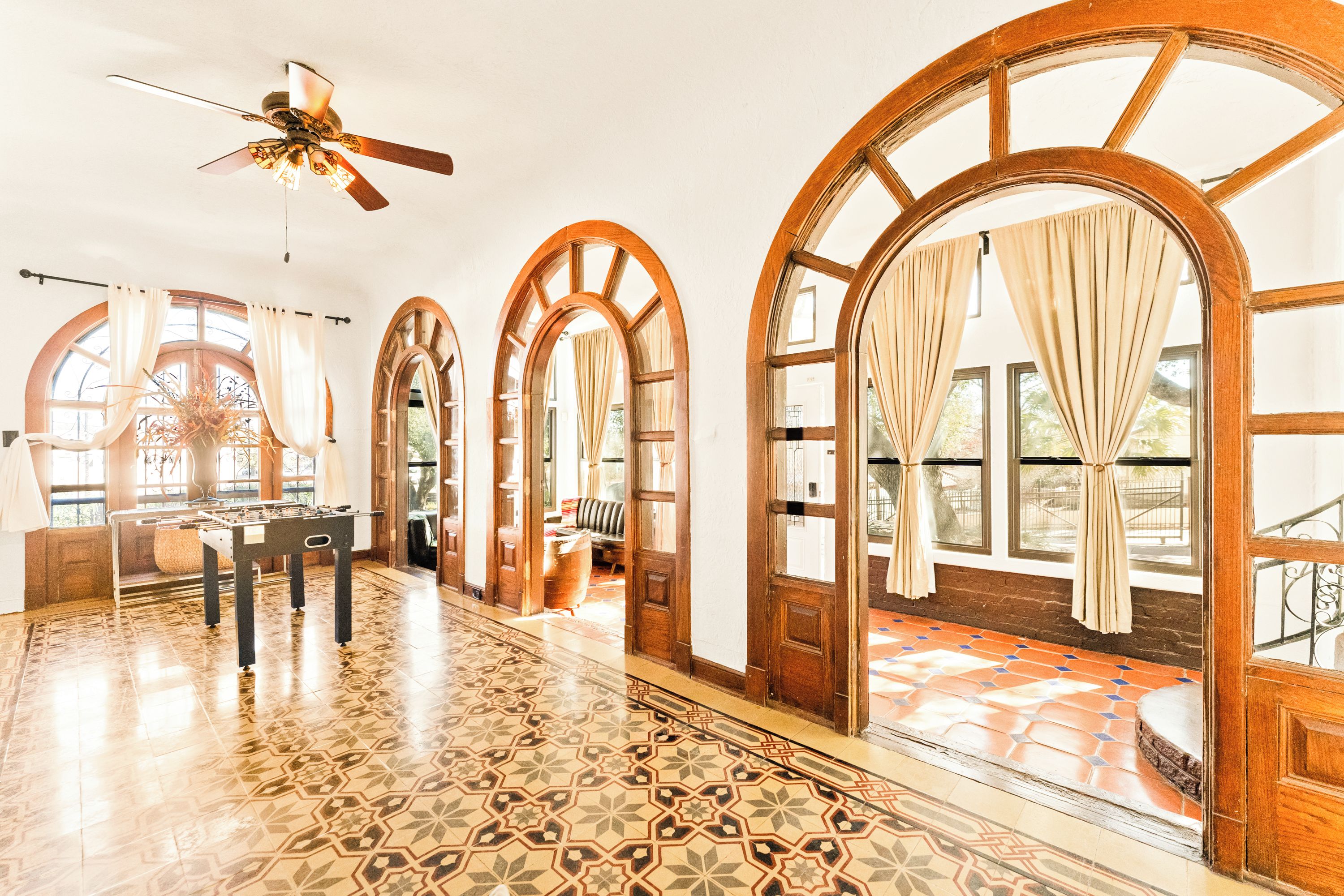 A spacious room with a patterned floor, large arched windows, and a ceiling fan.