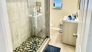Une salle de bain moderne avec une douche en verre, un lavabo avec un miroir et une fenêtre avec des stores.