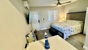 Une chambre à coucher avec un lit, un bureau avec une lampe, un ventilateur de plafond et une porte.