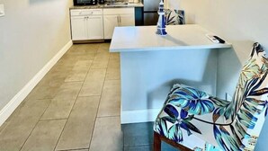 Une cuisine compacte avec des meubles blancs, un four à micro-ondes et un petit coin repas comprenant une table et une chaise à motifs.