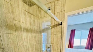Une douche avec une porte en verre, un sol carrelé et un pommeau de douche visible.