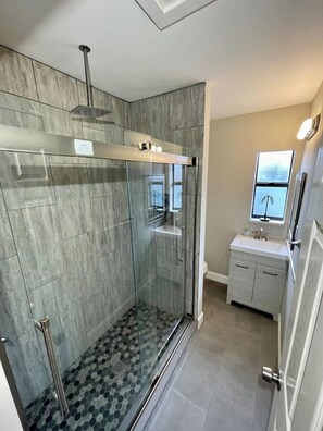 Un baño moderno con cabina de ducha de vidrio, tocador con espejo y suelo de baldosas.