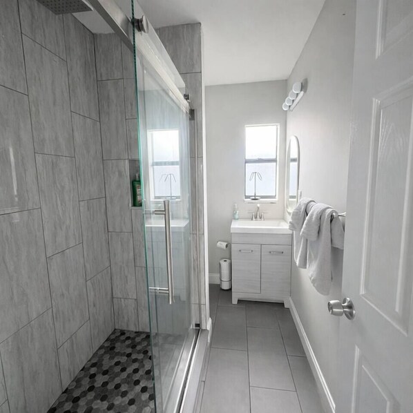 A modern bathroom with a glass shower enclosure, a sink, and a mirror.