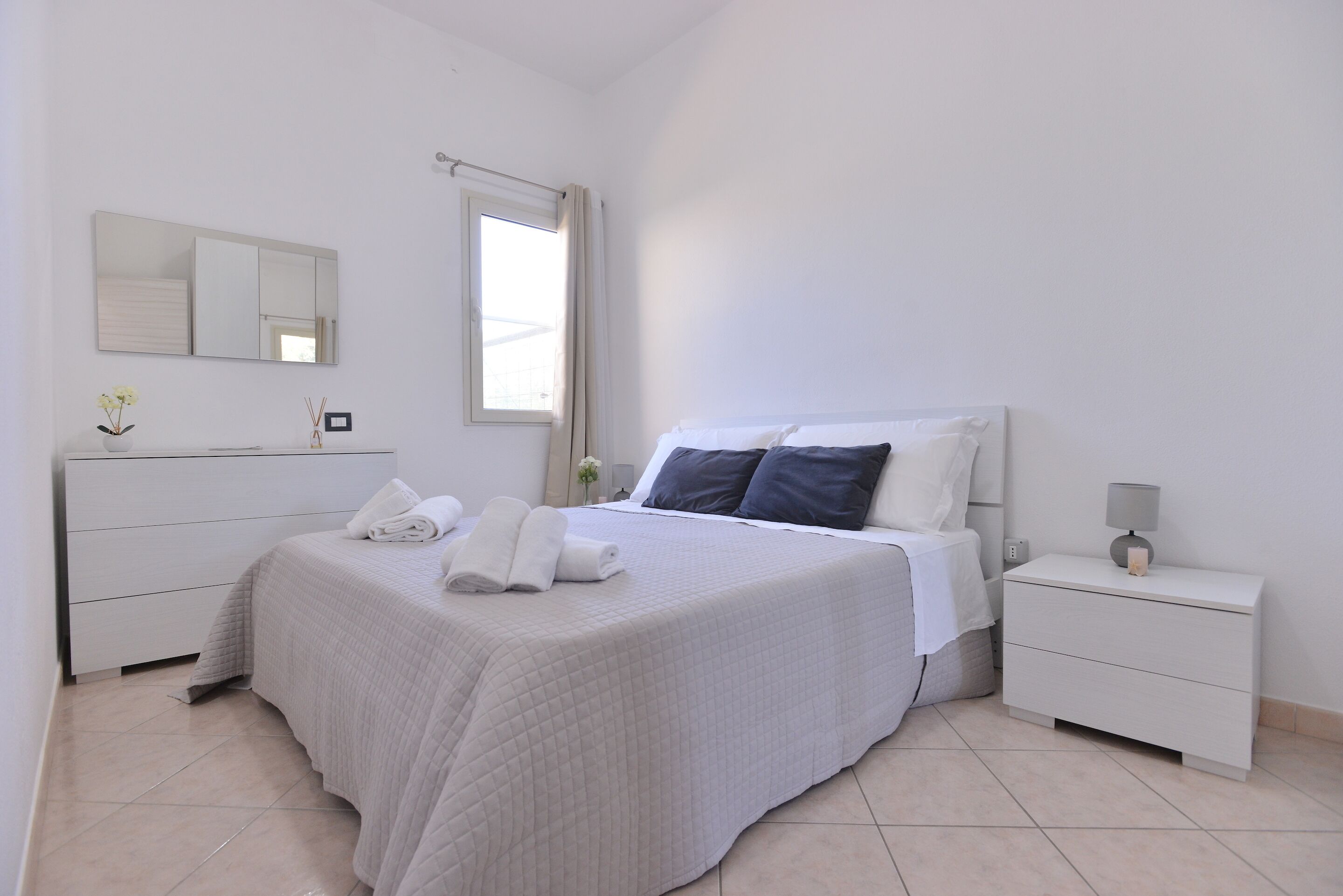 Une chambre à coucher bien rangée, avec un lit, des tables de chevet, un miroir et une fenêtre.