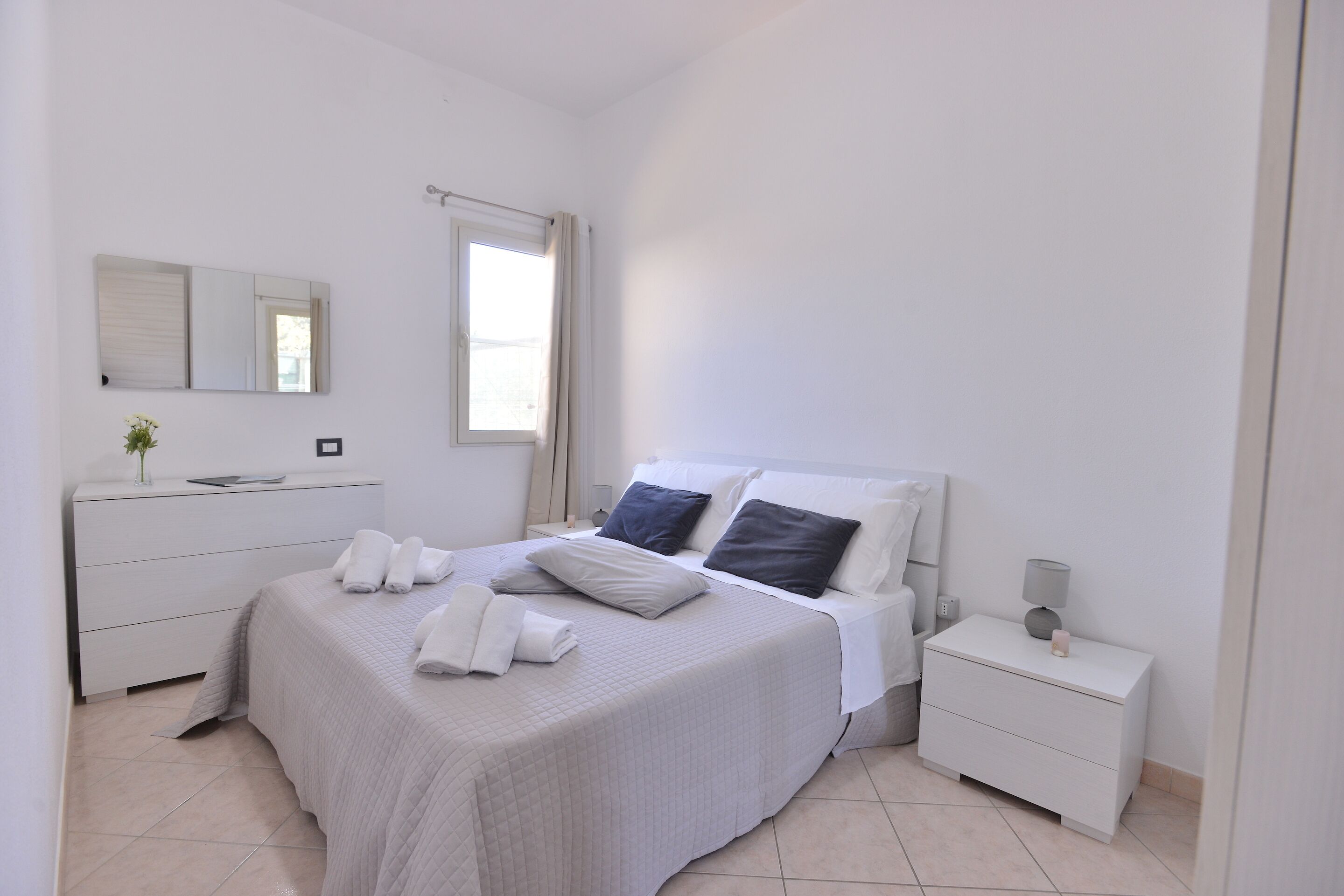 Un dormitorio ordenado con cama, mesitas de noche, cómoda y espejo.