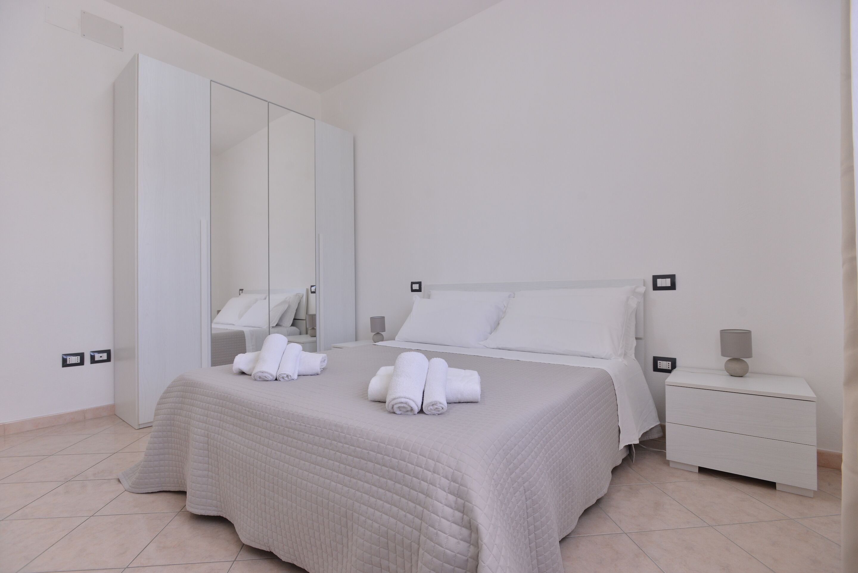 A bedroom with a bed, a nightstand, a mirror, and a wardrobe.