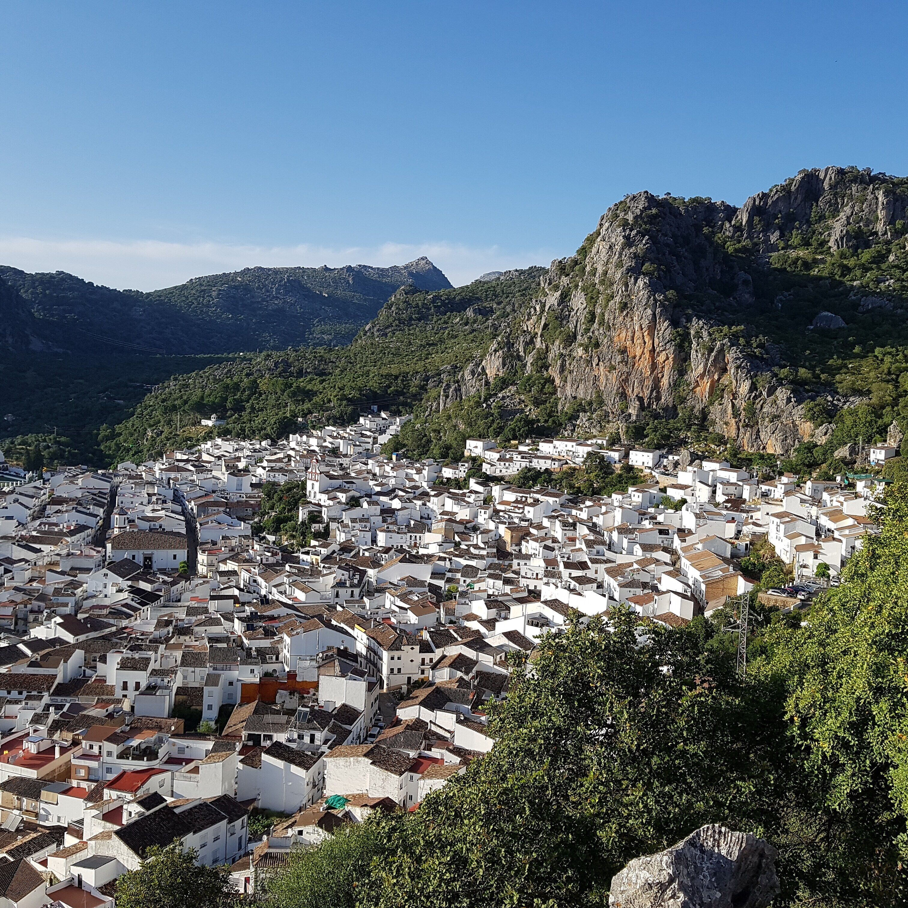 A coastal town with white buildings, a mountainous backdrop, and a clear sky.