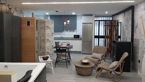 A modern kitchen with a dining area, a built-in oven, and a refrigerator. There are wicker chairs and a small table with a bowl. - Sierra Lof Paradise Apartment (Ubrique)