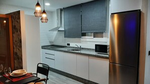 A modern kitchen with white cabinets, a stainless steel refrigerator, a microwave, and a dining area with a table and chairs. - Sierra Lof Paradise Apartment (Ubrique)