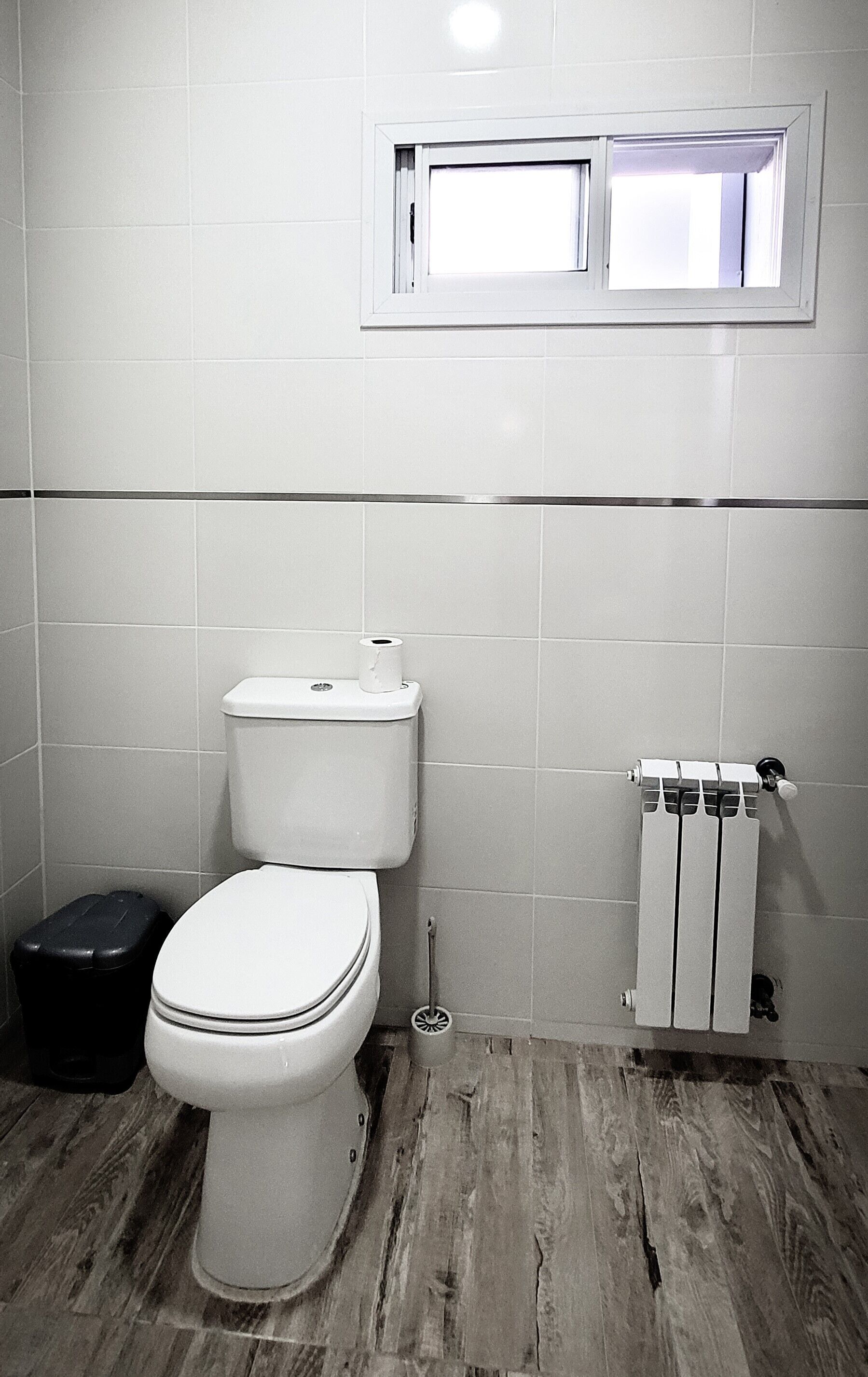 A bathroom with a toilet, a black trash bin, and a radiator.