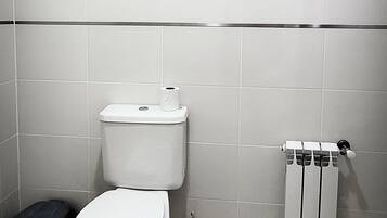 A bathroom with a toilet, a black trash bin, and a radiator.