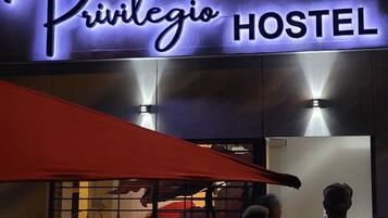 Das Äußere des Hostels Privilegio mit beleuchteter Beschilderung und zwei Außenleuchten.