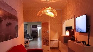 A modern living room with a red sofa, a hanging light fixture, a fireplace, and a television on the wall.