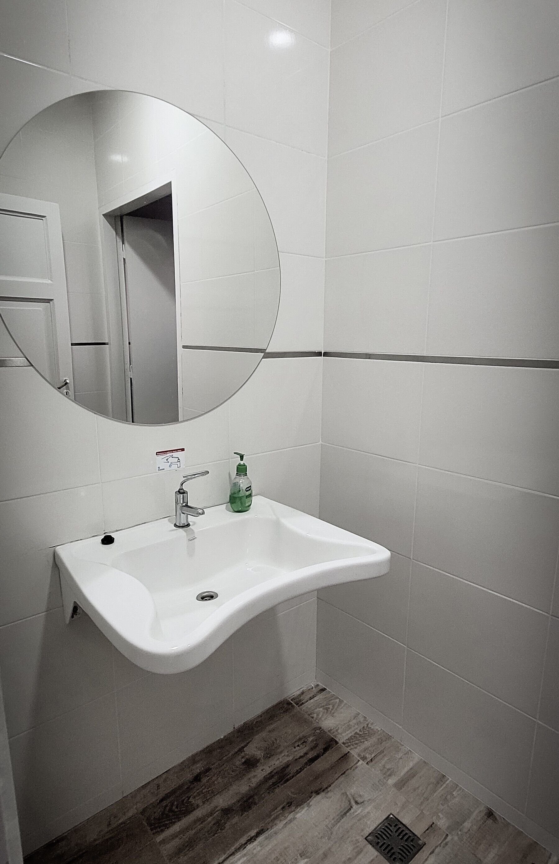 Une salle de bain avec un lavabo blanc, un miroir et un plancher en bois.