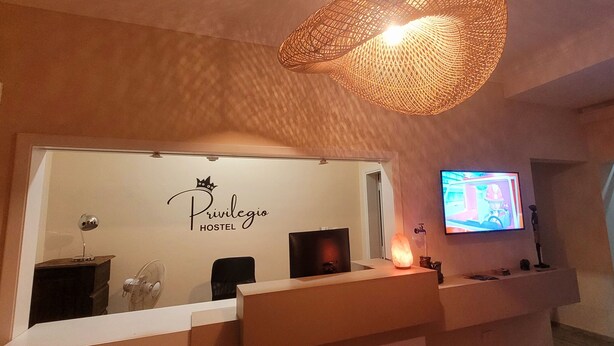 A reception area with a sign reading "Privilegio HOSTEL," a television mounted on the wall, and a large woven light fixture above the reception desk.