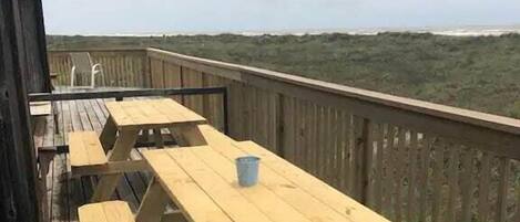 Una terraza de madera con mesas de picnic y vista a la playa.