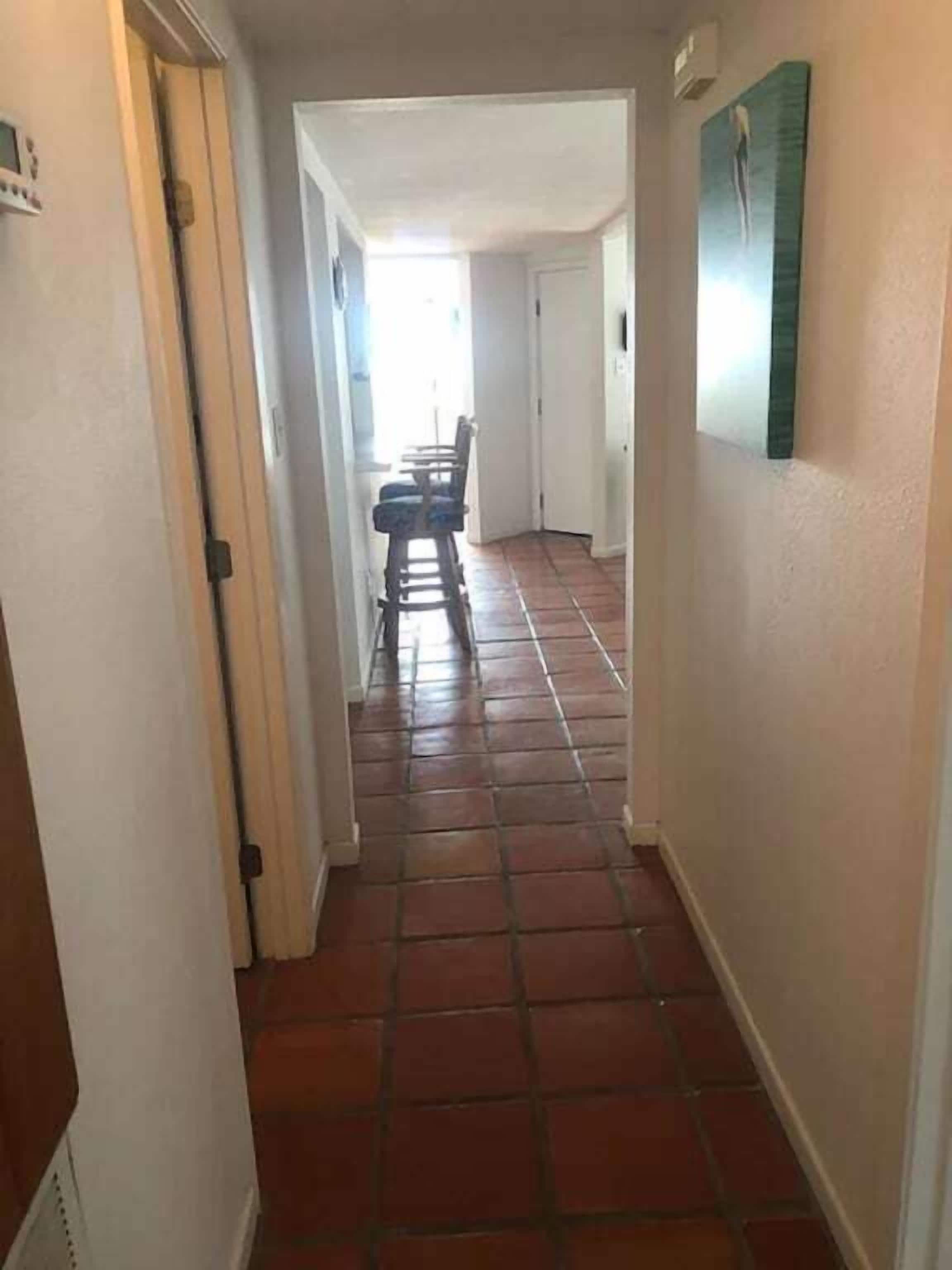 A narrow hallway with tiled flooring leading to a dining area with a table and chairs.