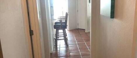 A narrow hallway with tiled flooring leading to a dining area with a table and chairs.