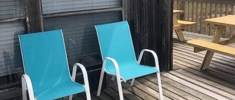 A wooden deck with two blue chairs and a picnic table.