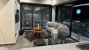 Un balcón moderno con puerta de cristal, sofá, mesa de comedor y televisor.