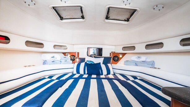 A spacious, well-lit interior with a large bed featuring blue and white striped bedding, a flat-screen TV mounted on the wall, and a small seating area with cushions.