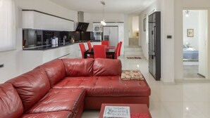 A modern living room with a red leather sofa, a dining area with red chairs, and a kitchen with white cabinets and stainless steel appliances. - Villa Blanka - Six Bedroom Villa with Swimming Pool and Sea View (Podgora)