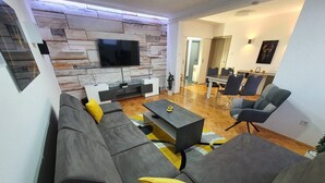 Una sala de estar moderna con pared de piedra, un televisor de pantalla plana, un conjunto de sofás, una mesa de centro y un comedor con sillas y una mesa.