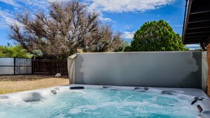 Ein Whirlpool mit Bedienfeld, umgeben von einer Holzdielen-Terrasse und einem Metallzaun.