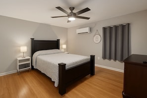 Une chambre à coucher comprenant un lit, des tables de chevet, un ventilateur de plafond, un climatiseur et une fenêtre avec des rideaux.