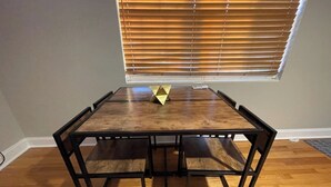Una mesa hexagonal con tapa de madera y estructura de metal negro, ubicada en una habitación con suelo de madera y una ventana con persianas.