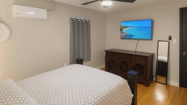 Un dormitorio con cama, cómoda, televisor y ventilador de techo.