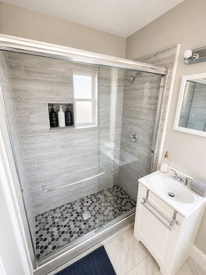 Une salle de bain moderne avec une douche à parois de verre, un lavabo blanc et un miroir.