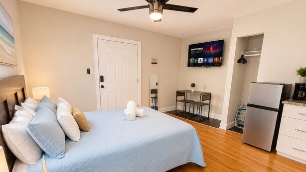 A hotel room with a bed, a desk, a refrigerator, a television, and a door. - Comfortable and Stylish Studio Near the Beach (Clearwater)