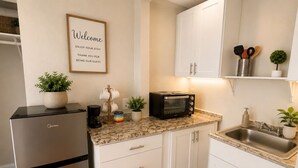 A modern kitchen with a refrigerator, microwave, and toaster. There is a welcome sign on the wall and a small plant on the counter. - Comfortable and Stylish Studio Near the Beach (Clearwater)