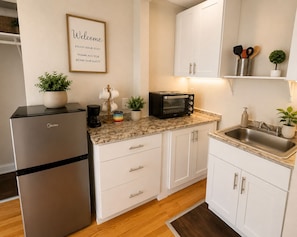 A modern kitchen with a refrigerator, microwave, and toaster. There is a welcome sign on the wall and a small plant on the counter. - Comfortable and Stylish Studio Near the Beach (Clearwater)