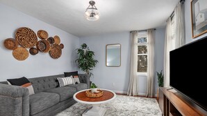 A living room with a grey sofa, a round coffee table, a flat-screen TV, and a large mirror on the wall. - Walk to Bridge Street from the Westside Charmer! (Grand Rapids)