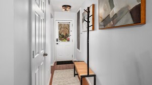 A hallway with a white door, a bench, a coat rack, and a framed abstract painting. - Walk to Bridge Street from the Westside Charmer! (Grand Rapids)
