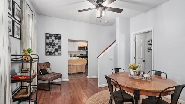 A dining area with a wooden table and chairs, a ceiling fan, and a kitchen in the background. - Walk to Bridge Street from the Westside Charmer! (Grand Rapids)