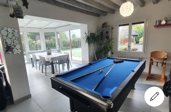 A pool table in a room with a dining area and large windows.