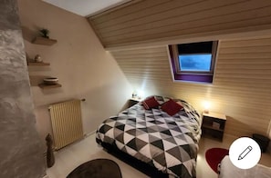A bedroom with a sloped ceiling, a bed with a geometric-patterned bedspread, a small window, and a radiator.