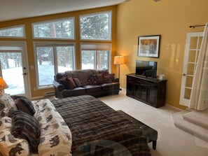 A bedroom with a large bed, a sofa, a TV, and a window with a view of trees.