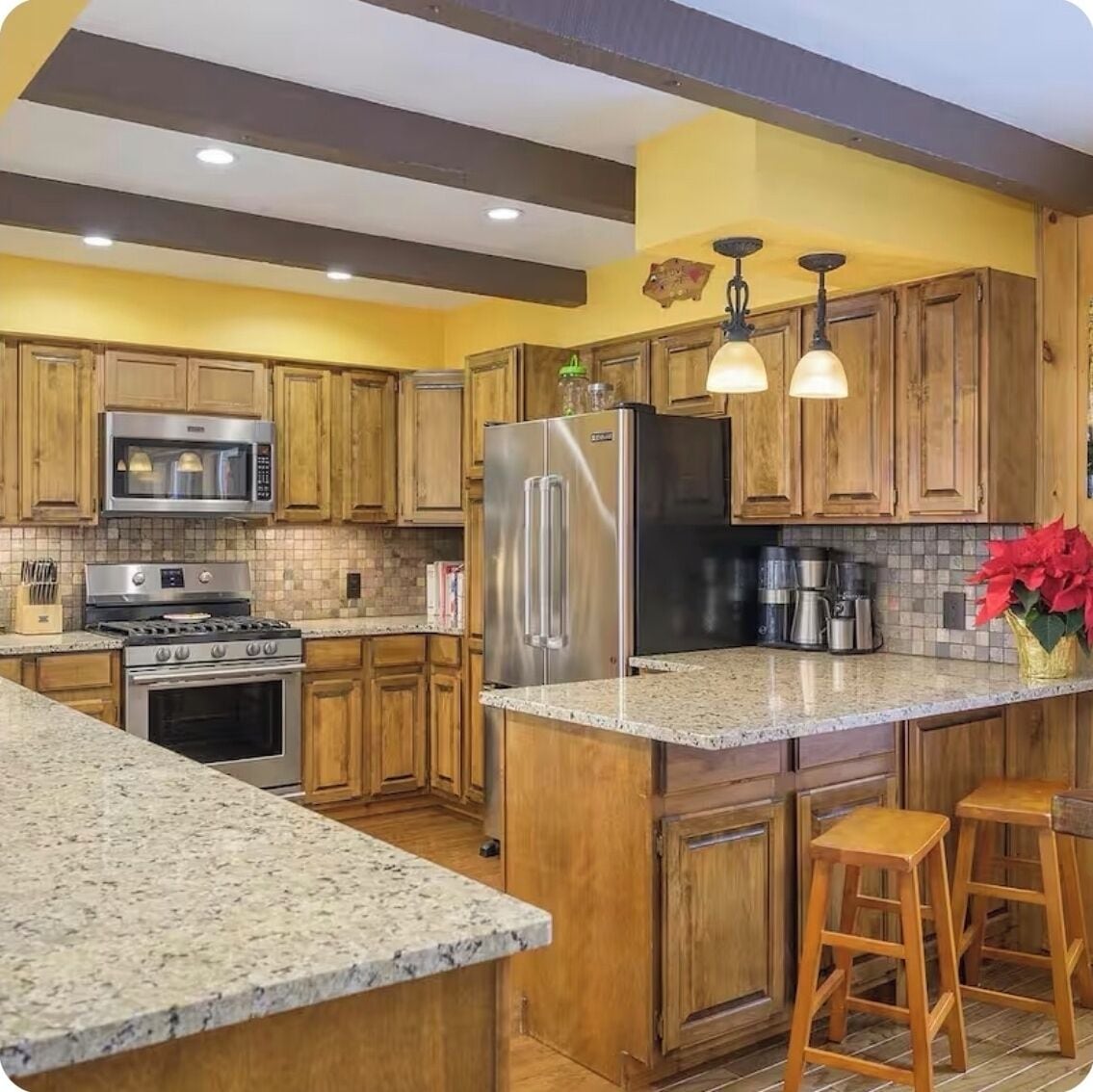 A kitchen with wooden cabinets, stainless steel appliances, granite countertops, and a central island with stools.
