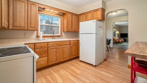 Una cocina con armarios de madera, un refrigerador blanco y un ventanal con vista a árboles.