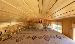 Ein Holzblock-Interieur mit einem Bett, einem Hängesessel und einem Fenster mit Blick.