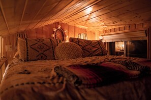 Acogedor dormitorio de cabaña de madera con cama, almohadas y chimenea.